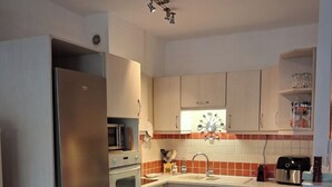 Cocina compacta con refrigerador, horno, microondas, pileta y un pequeño comedor con mesa y sillas.