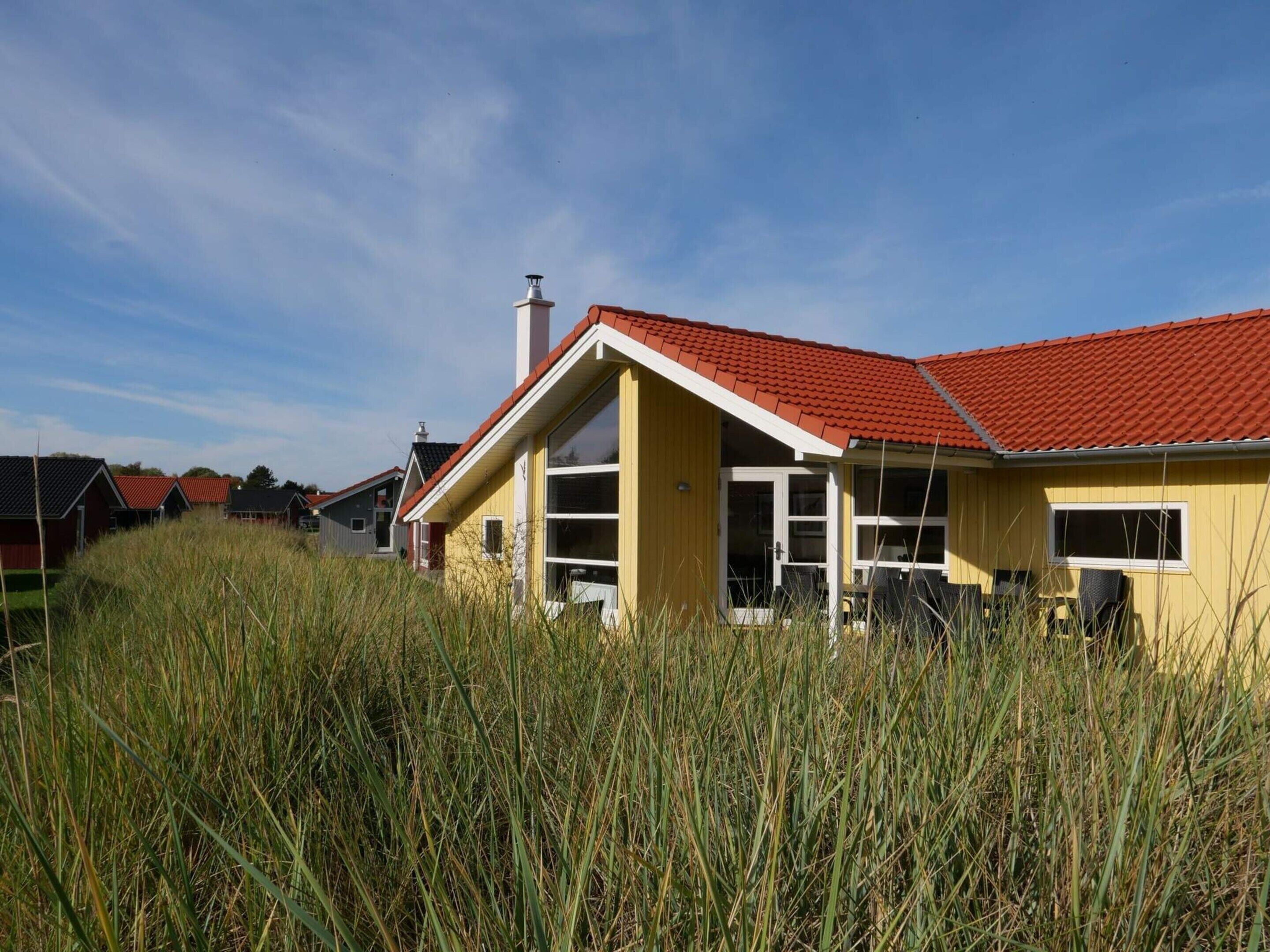 Un bâtiment jaune avec un toit rouge, entouré d’herbe haute.