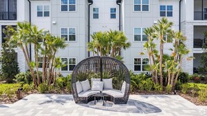 A modern building with a symmetrical facade, a circular outdoor seating area with cushions, and palm trees. - Pinnacle Apartments W Amenties by Heavenly Homes (Orlando)