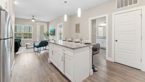 A modern kitchen with white cabinets, a granite countertop, and pendant lighting. - Pinnacle Apartments W Amenties by Heavenly Homes (Orlando)