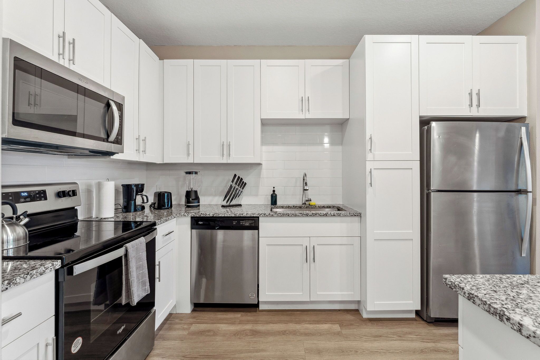 A modern kitchen with white cabinets, stainless steel appliances, a microwave, oven, dishwasher, and a refrigerator.