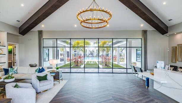 A spacious living area with a large window, a chandelier, and a reception desk. - Pinnacle Apartments W Amenties by Heavenly Homes (Orlando)