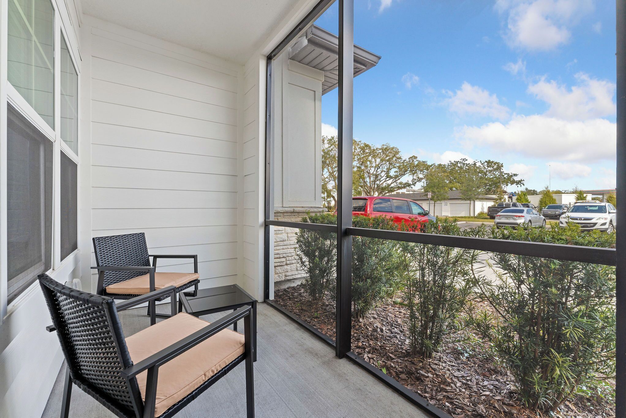 A balcony with two chairs and a table, overlooking a parking area with cars and greenery.