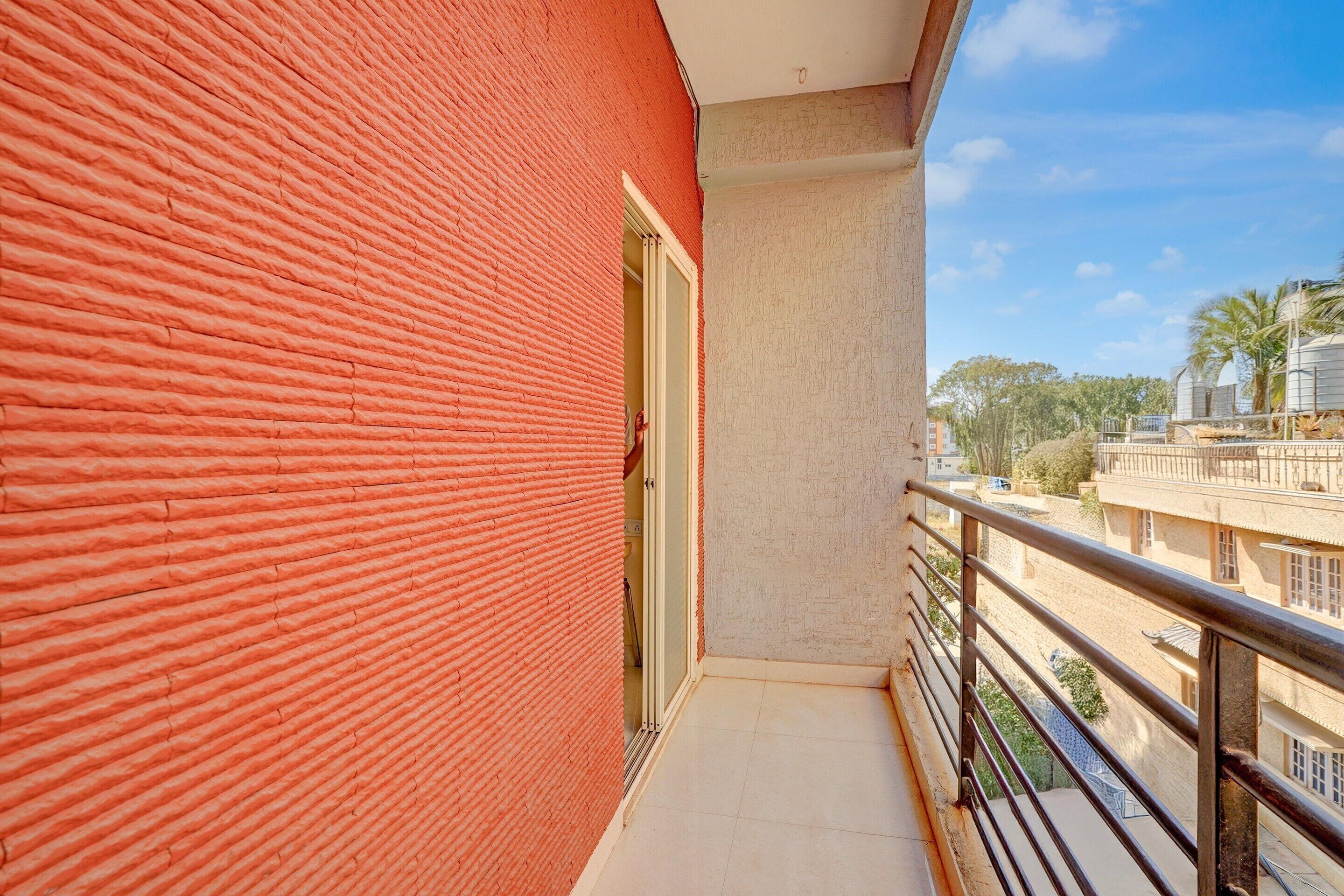 A balcony with a red wall, a white ceiling, and a view of a street with buildings and trees.