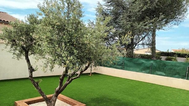 A garden with a tree in a wooden planter, a green lawn, and a fence. - Charming studio-cabin in quiet location near Nîmes and beaches (Bouillargues)