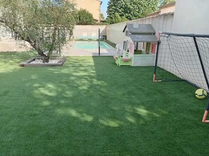 A backyard with artificial grass, a small tree, a playhouse, and a soccer goal. - Charming studio-cabin in quiet location near Nîmes and beaches (Bouillargues)