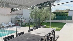 An outdoor patio with a wooden table and chairs, a pool, and a covered seating area. - Charming studio-cabin in quiet location near Nîmes and beaches (Bouillargues)