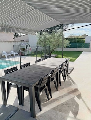 An outdoor patio with a wooden table and chairs, a pool, and a covered seating area. - Charming studio-cabin in quiet location near Nîmes and beaches (Bouillargues)