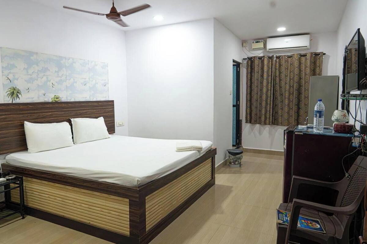 Quarto de hotel com cama, ventilador de teto, ar condicionado e escrivaninha com cadeira.