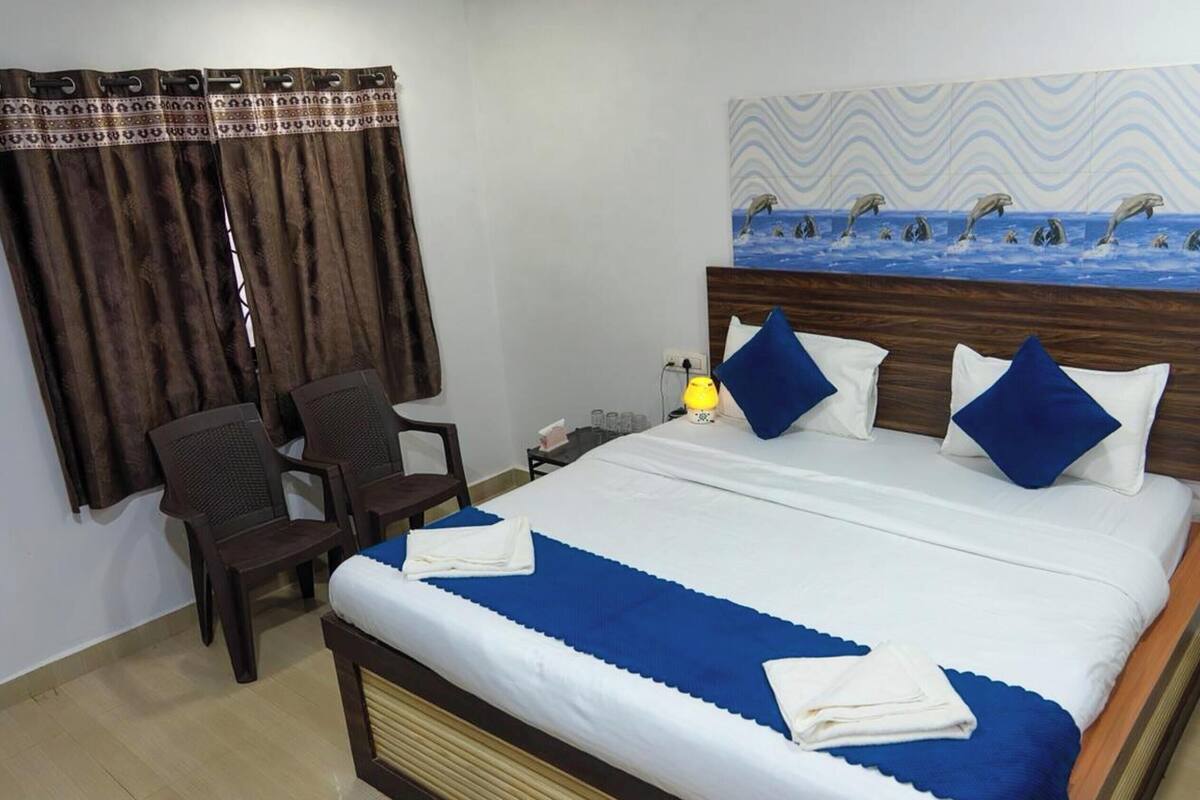 Quarto de hotel com cama, escrivaninha, cadeira, mesa de cabeceira e um quadro de golfinhos na parede.