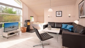 Ein modernes Wohnzimmer mit einer Couch, einem Sessel, einem Fernseher, einem Kamin und einem Esstisch.