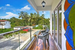 A balcony with a view of palm trees and a road, a chair, and a table. - Deluxe Celeb Da Luna (Chopdem)