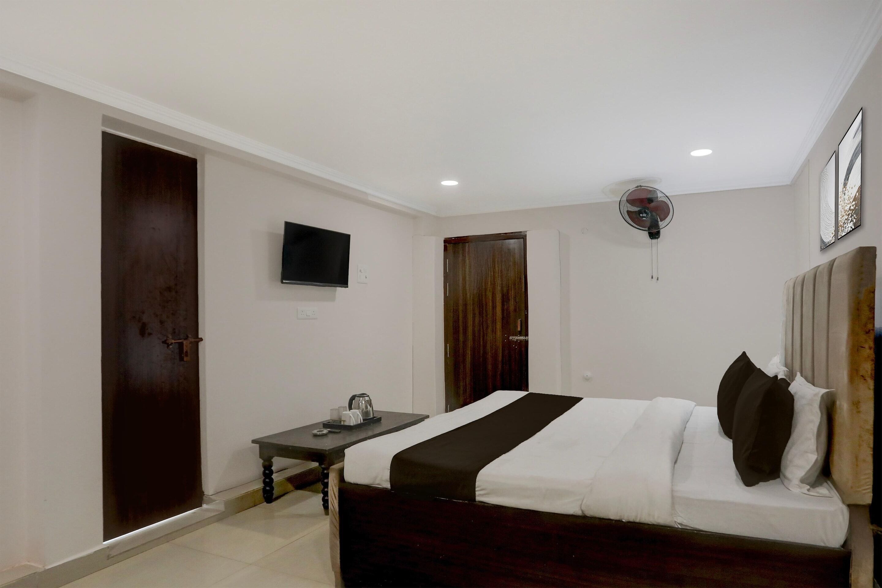 Una habitación de hotel con cama, escritorio, televisor, ventilador y una puerta.