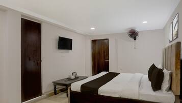 A hotel room with a bed, a desk, a TV, a fan, and a door.