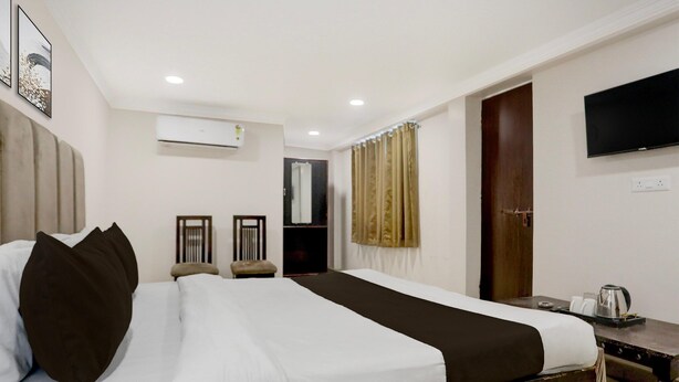 A hotel room with a bed, a television, an air conditioning unit, and a wooden desk with a kettle. - Deluxe Heritage Hotel (Prayagraj)