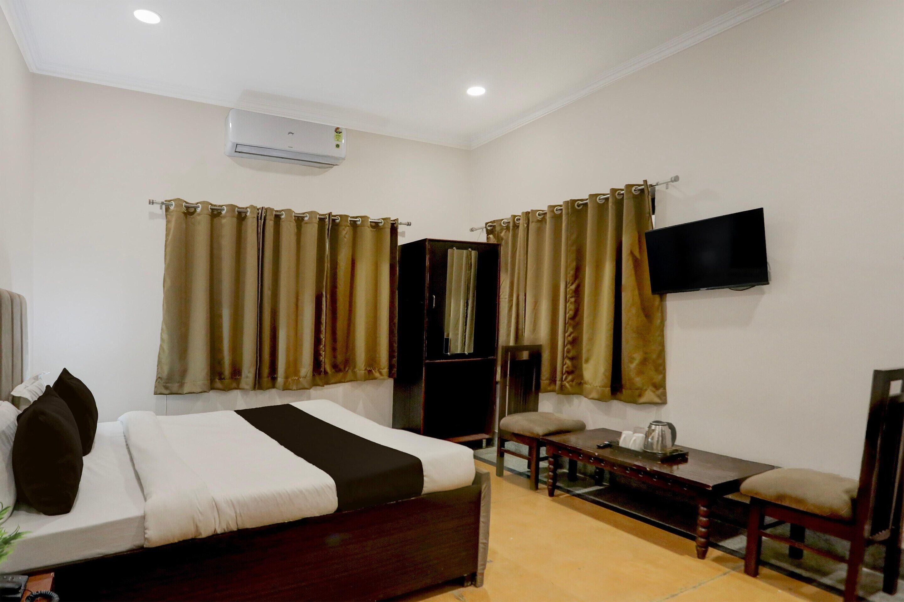 Una habitación de hotel con cama, escritorio, silla, televisor y aire acondicionado.