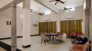 A spacious room with a high ceiling, a round table with chairs, a sofa, and a ceiling fan. - Deluxe Heritage Hotel (Prayagraj)