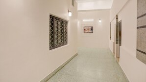 A corridor with a tiled floor, a window with a geometric pattern, and a framed picture on the wall. - Deluxe Heritage Hotel (Prayagraj)