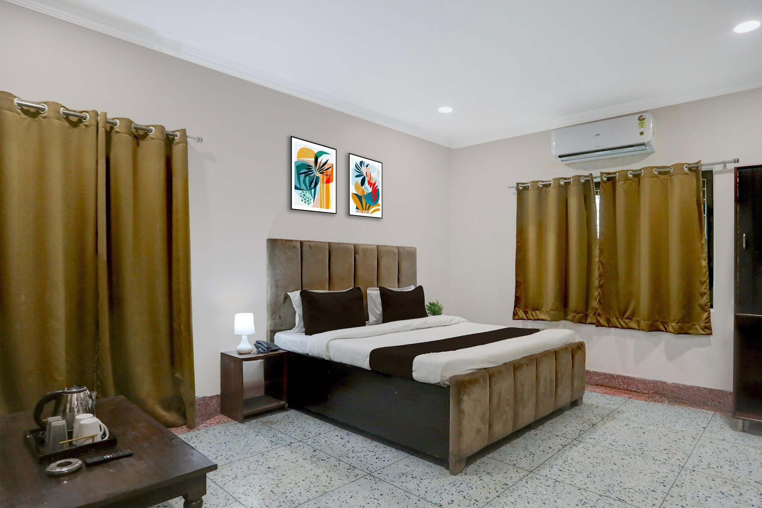A bedroom with a bed, curtains, a bedside table with a lamp, and artwork on the wall.