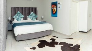 A bedroom with a bed, a headboard, a wall-mounted air conditioning unit, a door, and a cowhide rug. - Tree Tops Game Resort Eswatini  (Big Bend)