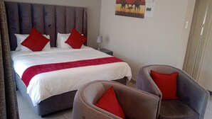 A hotel room with a bed, two nightstands, a lamp, and two armchairs. - Tree Tops Game Resort Eswatini  (Big Bend)