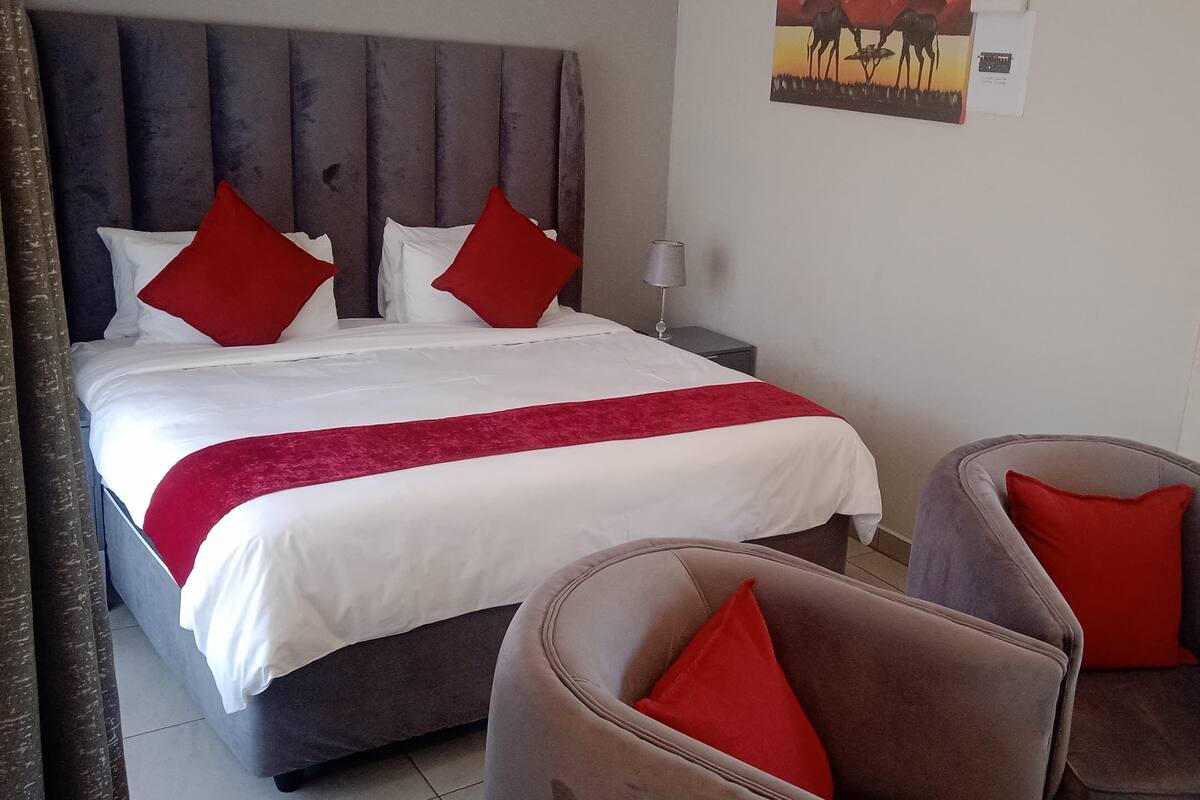 Una habitación de hotel con una cama, dos mesitas de noche, una lámpara y dos sillones.