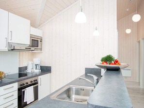 A modern kitchen with white cabinets, a built-in microwave, a stove, a sink, and pendant lighting. - 4 Star Holiday Home in Grossenbrode (Grossenbrode)