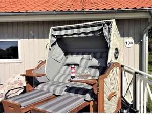 A covered outdoor seating area with a cushioned bench, a small table with a bottle, and a window. - 4 Star Holiday Home in Grossenbrode (Grossenbrode)