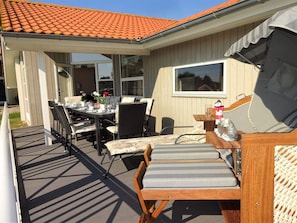 A covered patio with a dining table and chairs, a cushioned bench, and a window overlooking the deck. - 4 Star Holiday Home in Grossenbrode (Grossenbrode)