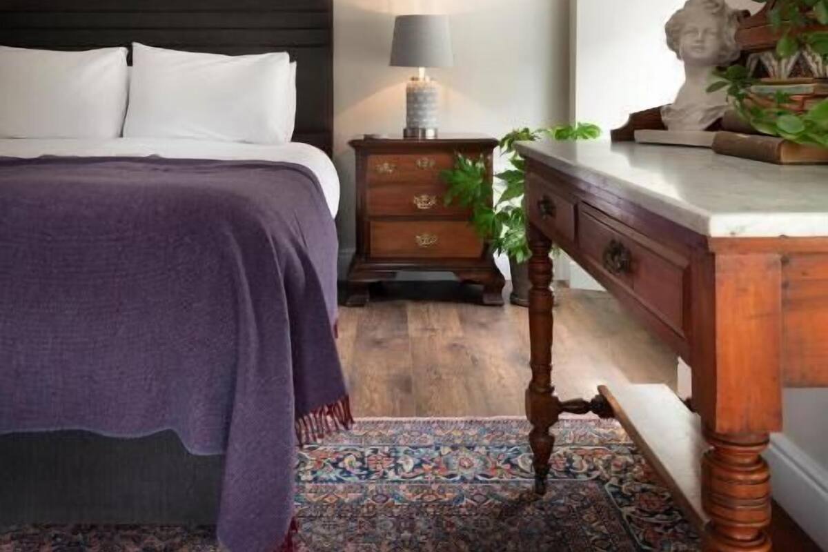 A bedroom with a bed, a nightstand, a dresser, a lamp, and a bust on the dresser.