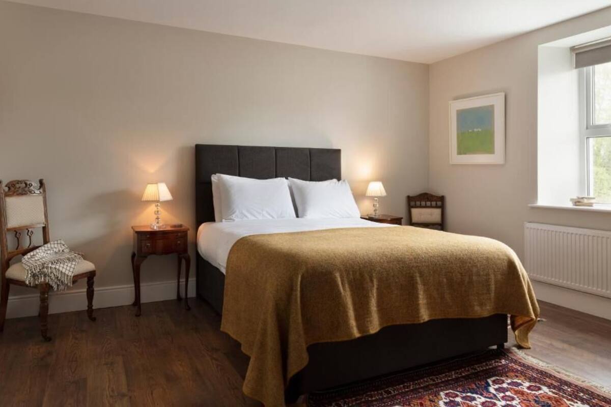A bedroom with a bed, two bedside tables, a chair, a window with a view, and a radiator.