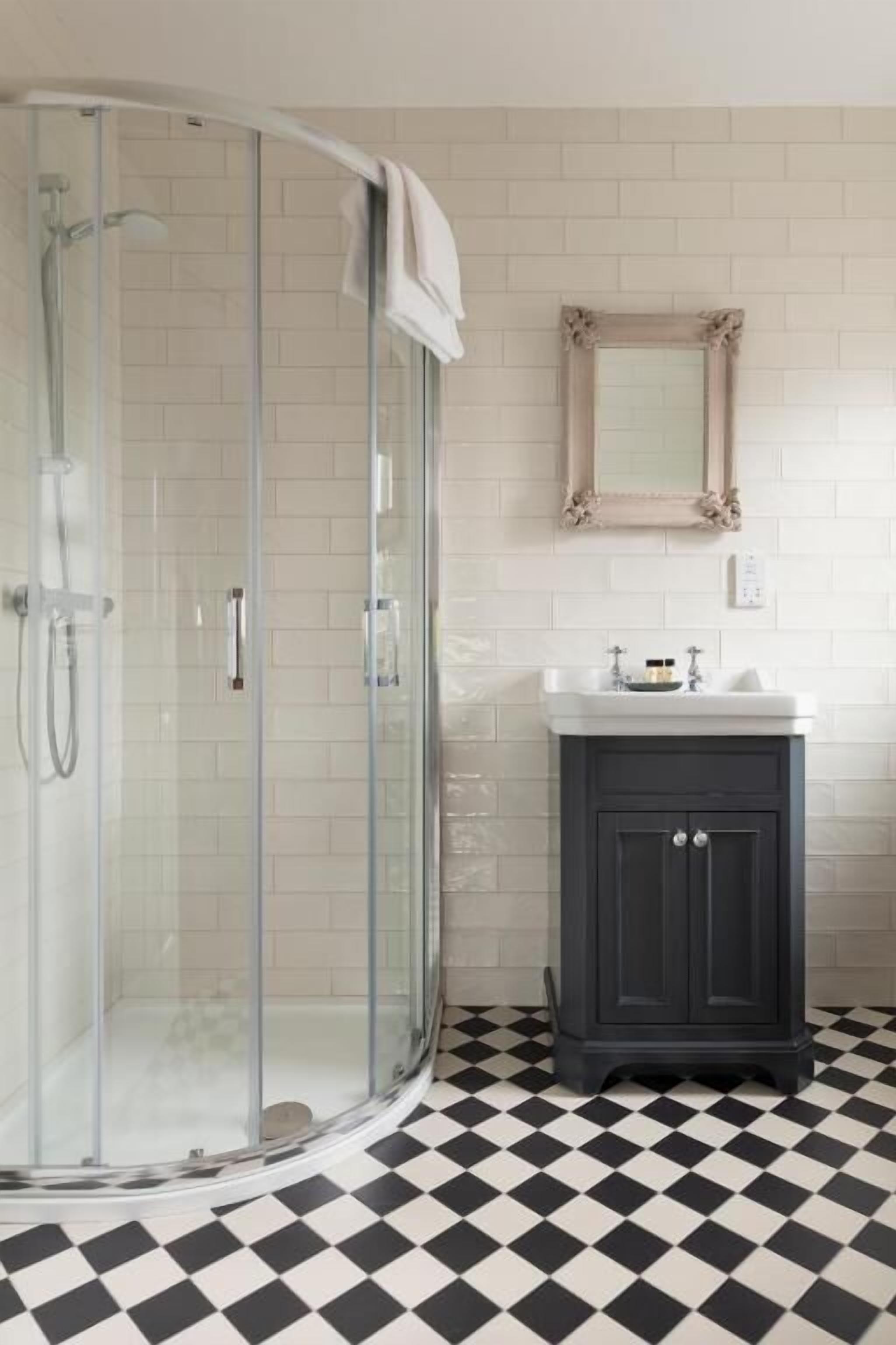 A bathroom with a glass-enclosed shower, a white sink with a dark cabinet, and a checkered floor.