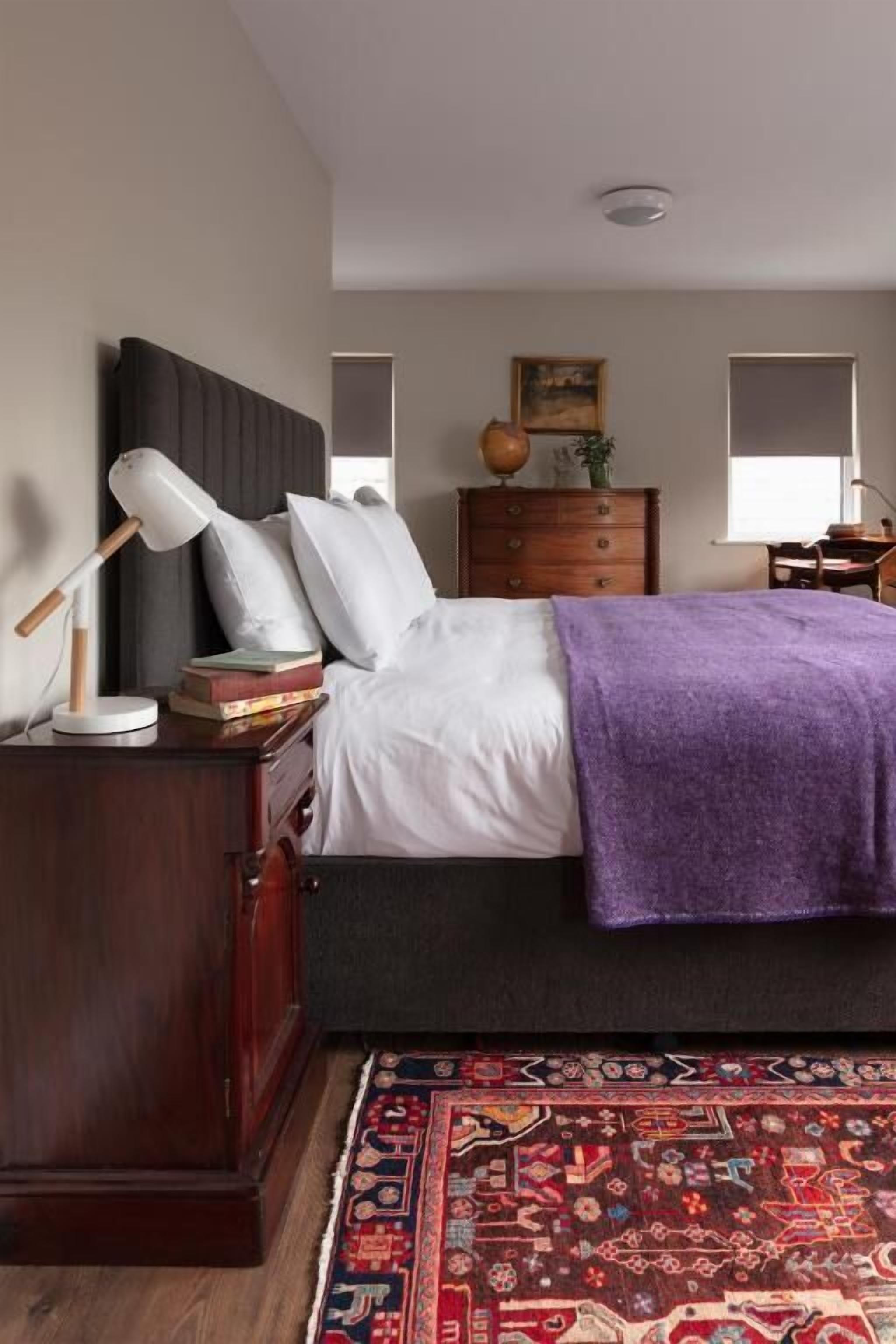 A bedroom with a bed, a nightstand, a lamp, a dresser, and a rug.
