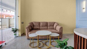 A room with a beige wall, a brown sofa, three round tables with gold legs, and a potted plant. - Deluxehotel Pratee Heights (Bhubaneshwar)