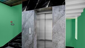 A marble elevator in a green-walled hallway with a staircase. - Deluxehotel Pratee Heights (Bhubaneshwar)