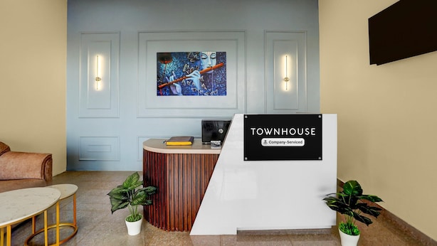 A reception area with a wooden desk, a sign reading 'TOWNHOUSE Company-Serviced,' and a painting on the wall. - Deluxehotel Pratee Heights (Bhubaneshwar)