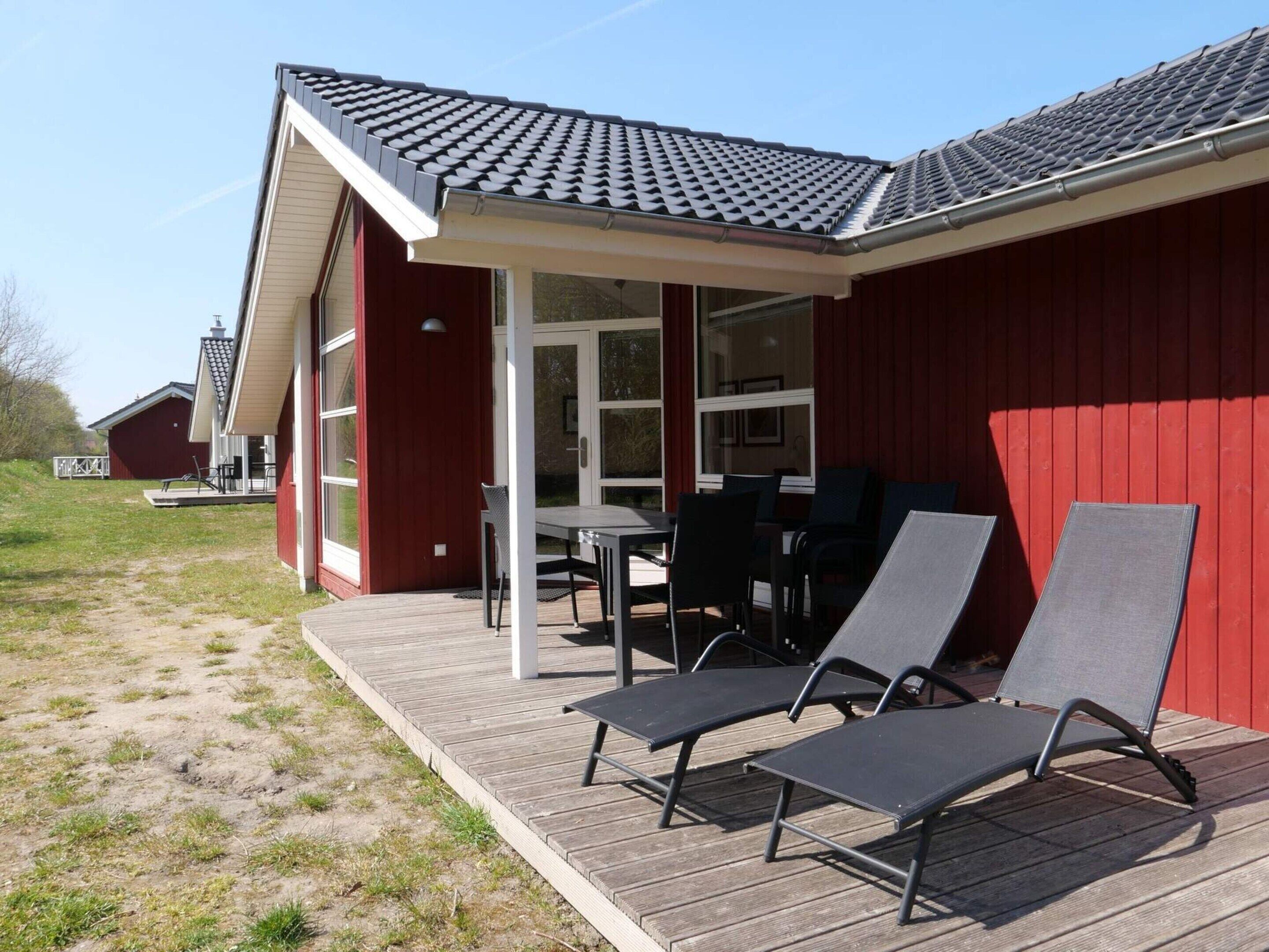 Ein rotes Gebäude mit überdachter Terrasse, Außenbestuhlung und einer Holzterrasse.