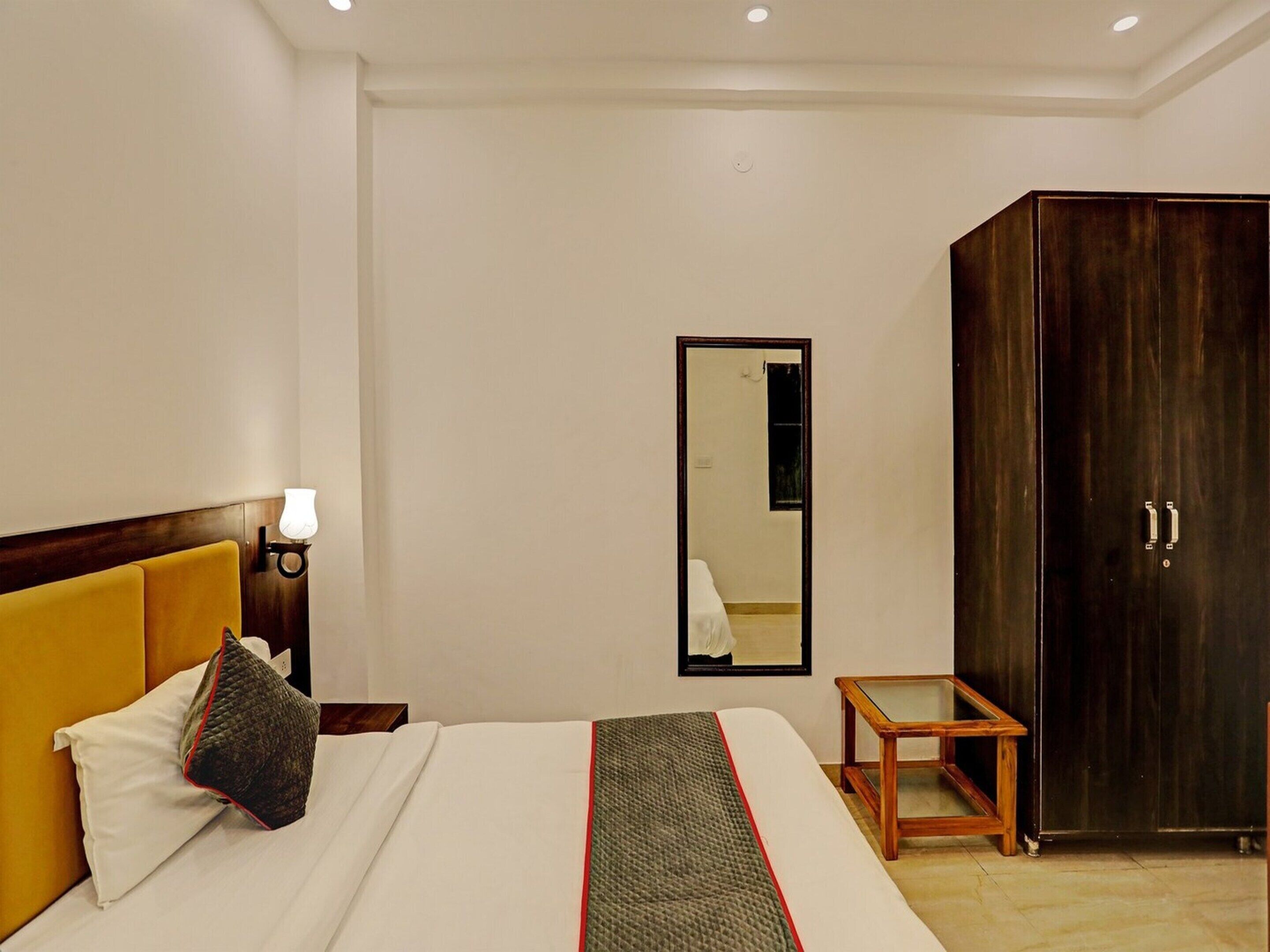 A hotel room with a bed, a nightstand, a lamp, a mirror, a wardrobe, and a small table.