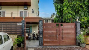 Une entrée fermée par un portail, avec une voiture garée devant, un immeuble doté d’un balcon et un arbre en arrière-plan.