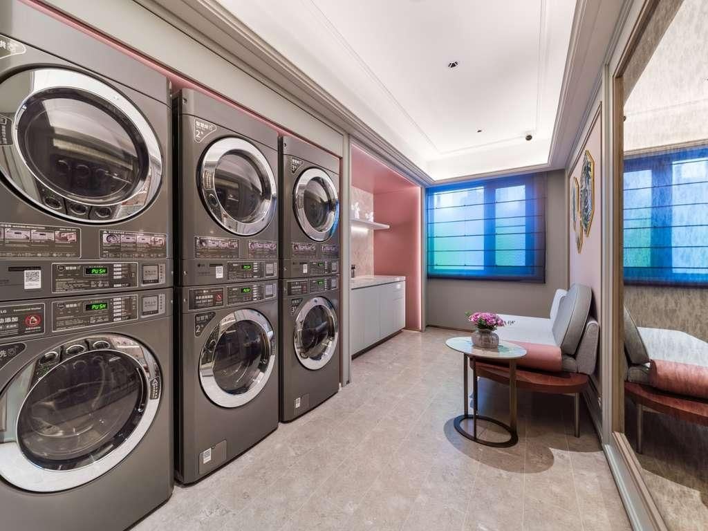 A laundry room with four stacked washing machines, a small table with a vase, and a window with blue-tinted glass.