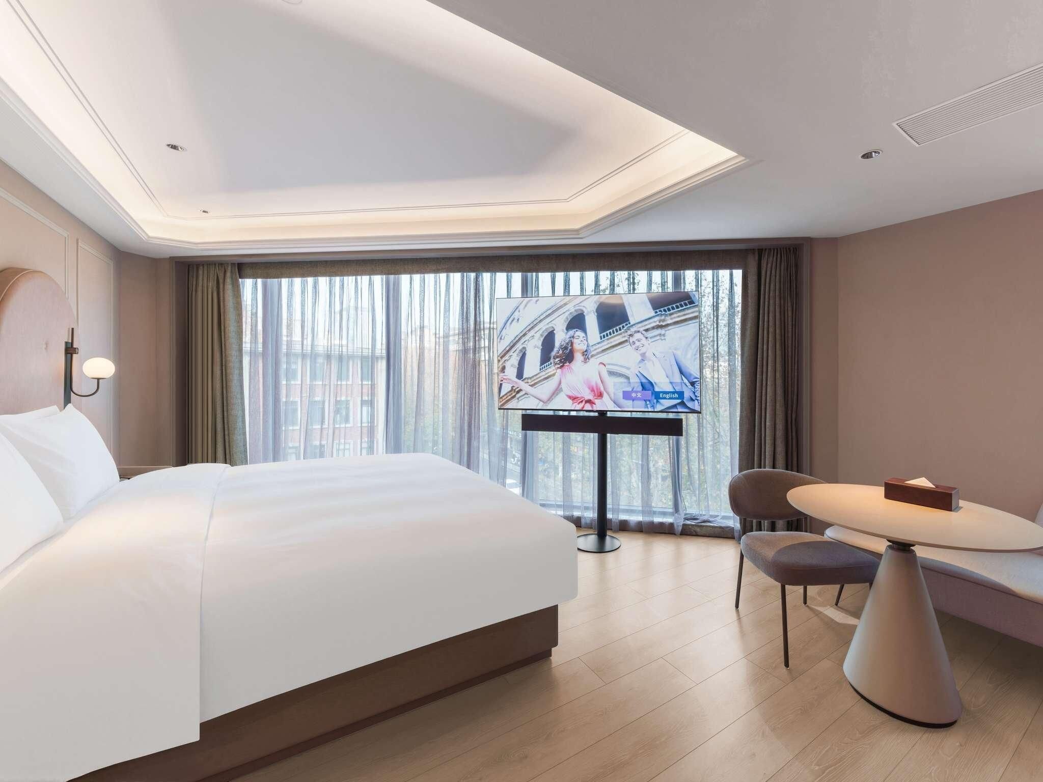 A hotel room with a large bed, a TV, a dining table, and a chair.