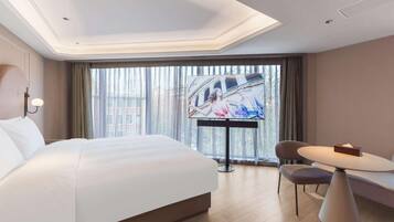 A hotel room with a large bed, a TV, a dining table, and a chair.