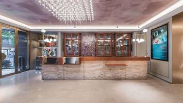 A reception area with a marble counter, a chandelier, and a digital screen displaying information.
