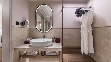 A modern bathroom with a large oval mirror, a round sink, and a wooden bench.
