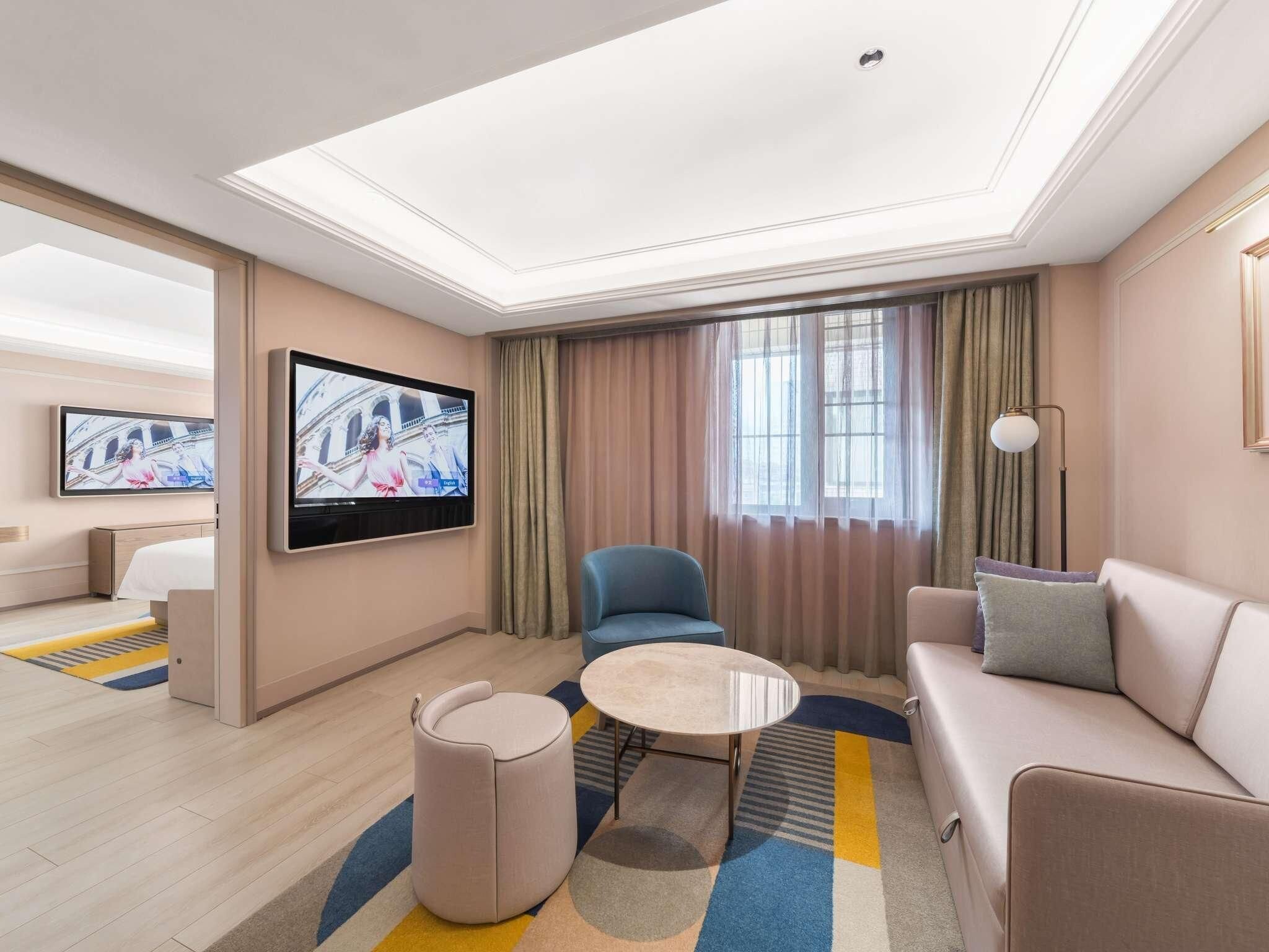 A hotel room with a flat-screen TV, a sofa, a chair, a small table, and a bed.