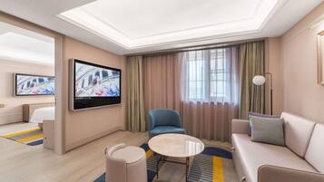 A hotel room with a flat-screen TV, a sofa, a chair, a small table, and a bed.