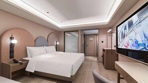 Quarto de hotel com cama, mesa de cabeceira, televisão e escrivaninha com cadeira.