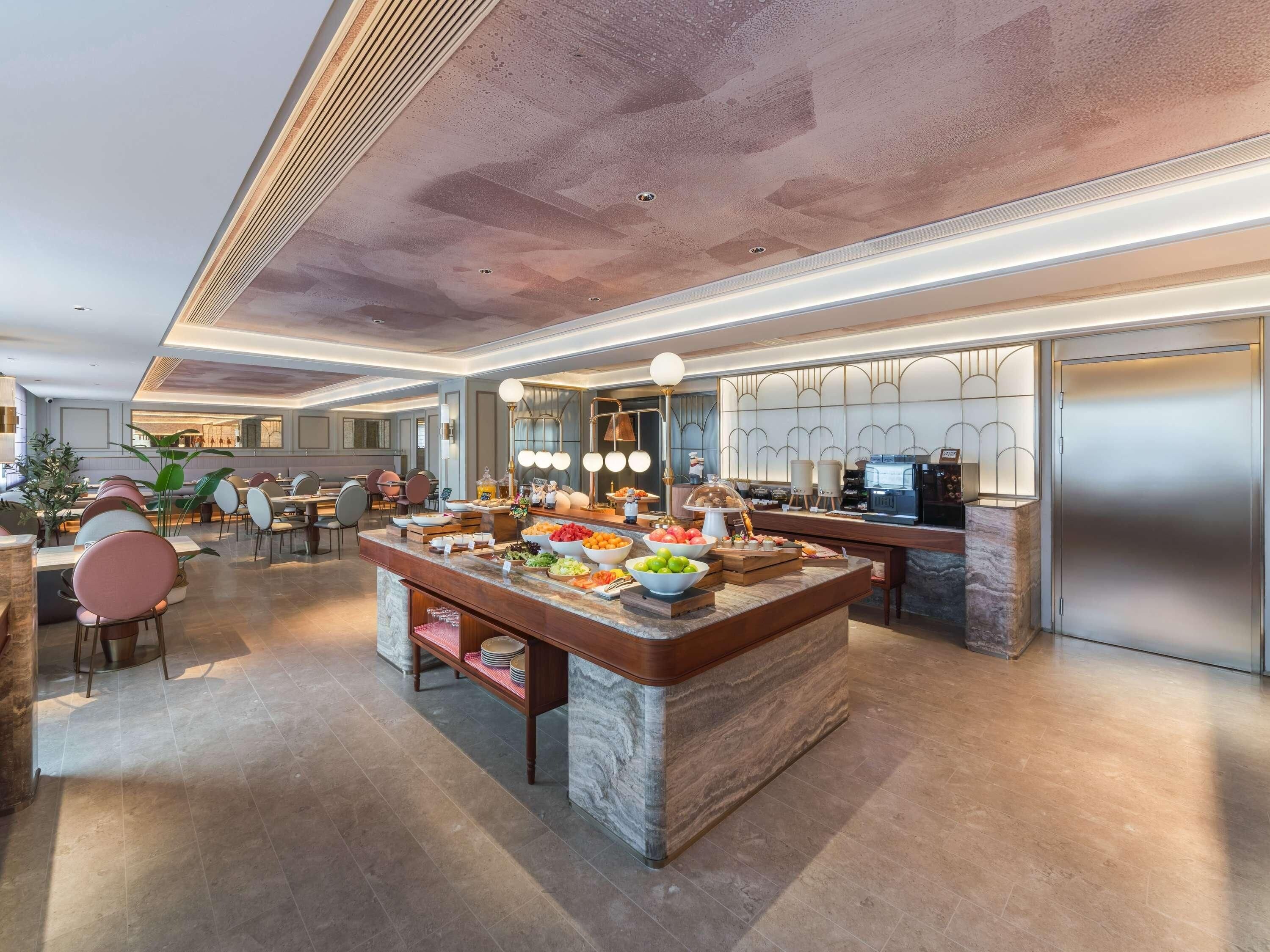 A modern kitchen with a marble island, stainless steel appliances, and a dining area with chairs and tables.