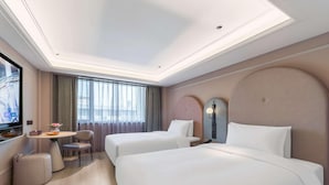 Quarto de hotel com duas camas, televisão, escrivaninha com cadeira e uma janela grande com cortinas.