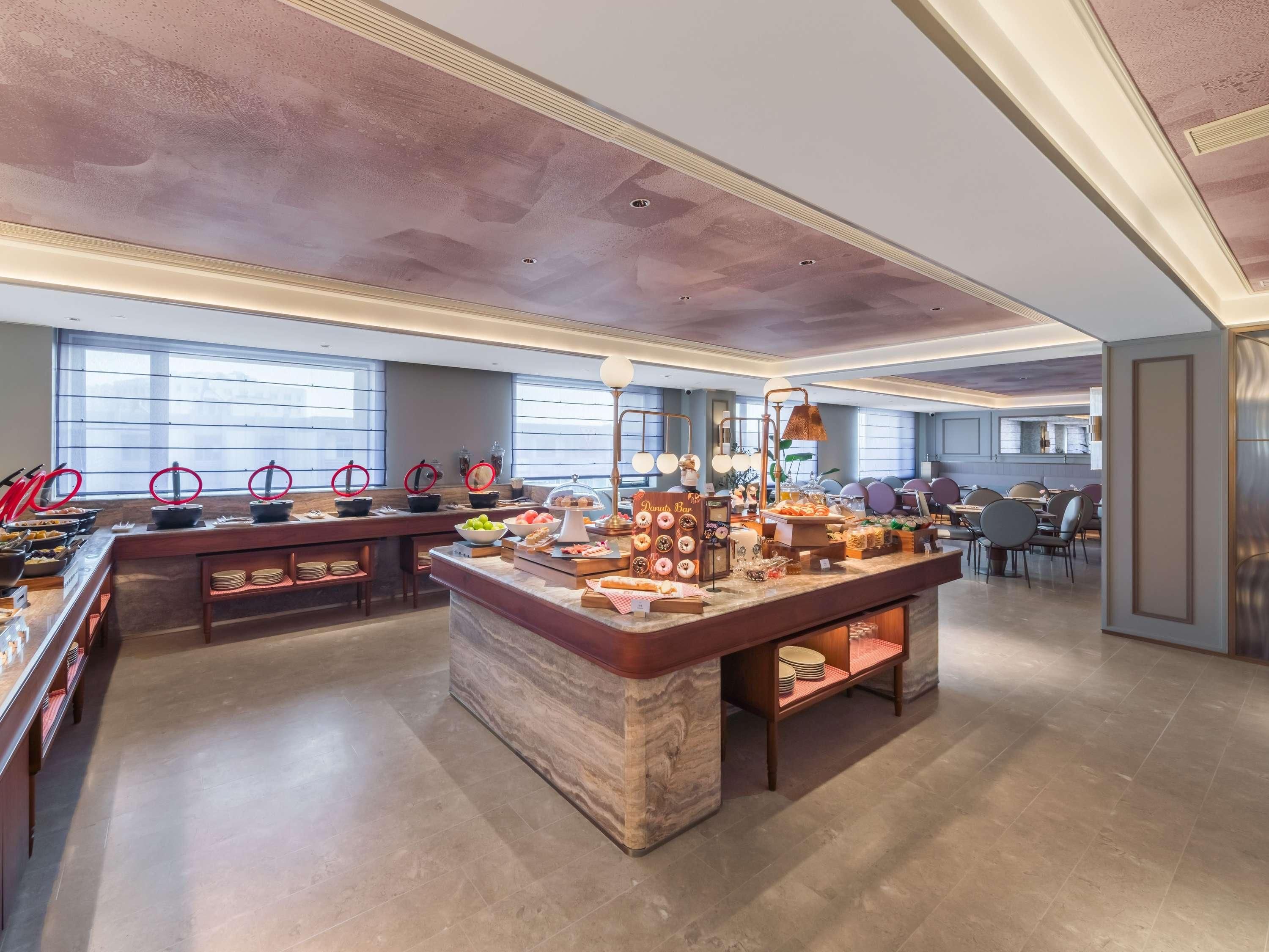 A spacious hotel dining area with multiple seating arrangements and a central buffet station.
